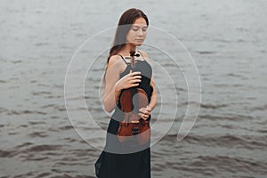 beautiful brown-haired girl of Asian appearance with a violin in nature. musician in nature. classical music