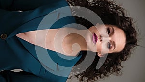 Beautiful brown-haired girl with a perfectly curly flying hair, classic make-up and a blue suit. Beauty face and hair.