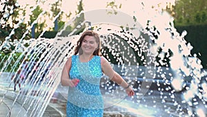 Beautiful brown-haired woman cheerfully runs under the fountains and laughs Slow motion