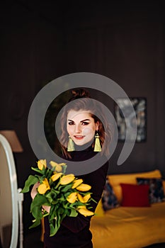 A beautiful brown-haired woman in purple clothes holds a bouquet of yellow tulips in her hands , on a dark background in