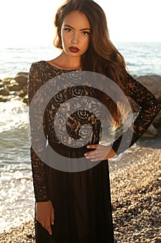 Beautiful brunette in black lace dress posing on beach