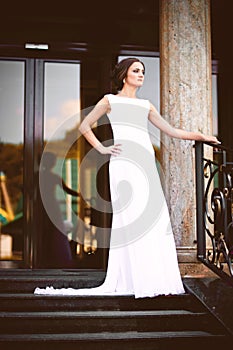 Beautiful brunette bride in white dress walking up stairs