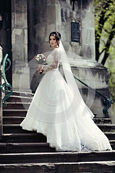 Beautiful brunette bride in white dress walking up stairs,
