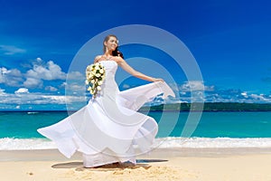 Beautiful brunette bride in white wedding dress with big long white train and with wedding bouquet stand on shore sea. Tropical s