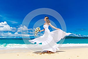 Beautiful brunette bride in white wedding dress with big long white train and with wedding bouquet stand on shore sea. Tropical s