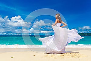 Beautiful brunette bride in white wedding dress with big long white train and with wedding bouquet stand on shore sea. Tropical s