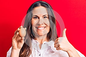 Beautiful brunette businesswoman holding bunch of dollars banknotes over red background smiling happy and positive, thumb up doing