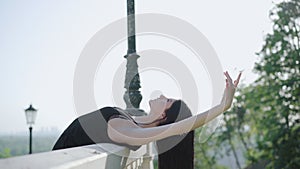 Beautiful brunette Caucasian woman bending over stairs handrails on sunny day. Side view portrait of young ballerina