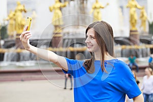 Beautiful brunette dress taking pictures of herself on a cellphone in a city park