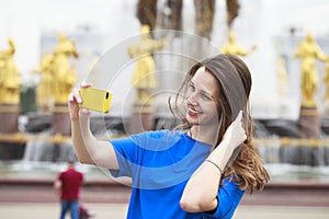 Beautiful brunette dress taking pictures of herself on a cellphone in a city park