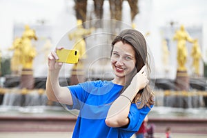 Beautiful brunette dress taking pictures of herself on a cellphone in a city park