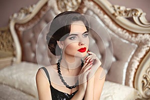 Beautiful brunette, elegant woman portrait. Manicure nails. Retro lady with red lips makeup, wavy hairstyle posing on modern bed