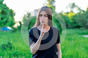 Beautiful brunette European girl. In summer in the park in nature. Emotionally shows a gesture quietly. With a gesture