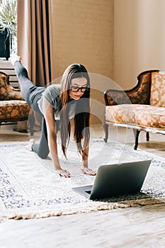 Beautiful brunette fitness woman make stretching exercises in front laptop doing yoga indoors at home. Staying fit and healthy