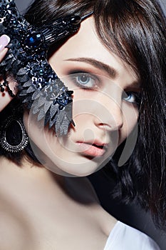 Beautiful brunette girl with big blue eyes holding a black brooch decoration in the form of birds. Fashion portrait natural makeup