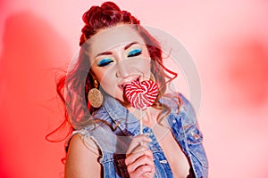 Beautiful brunette girl with blue makeup, pigtails and a sleeveless denim vest posing on a red background with a heart-shaped