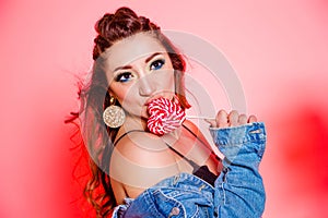 Beautiful brunette girl with blue makeup, pigtails and a sleeveless denim vest posing on a red background with a heart-shaped