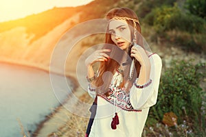 Beautiful brunette girl in Bocho chic style stands on the background of the sea in the rays of a bright sun. Vintage color tone