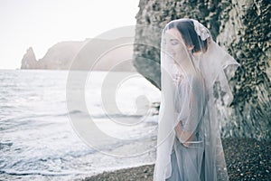 Beautiful brunette girl bride in a grey gown of lace and tulle, covered her face with a veil, hand on breast