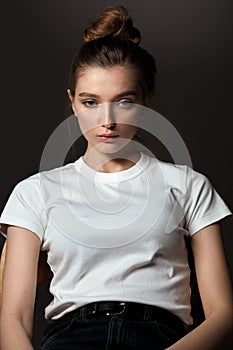 Beautiful brunette girl with bunched hair dressed in white t-shirt and jeans poses on the black background in the studio