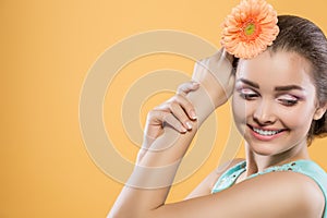 Beautiful brunette girl with closed eyes on a yellow background. Woman holds gerbera flower near the head. Close-up.