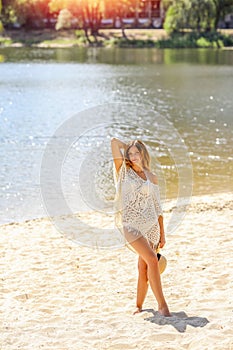 A beautiful brunette girl with curls walks on the beach. Knitted white pareo and hat