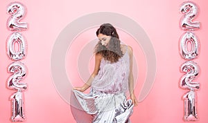 Young woman on a pink background with silver balls in the form of the numbers 2021 photo