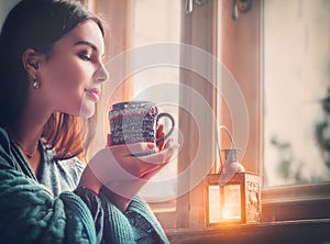 Beautiful brunette girl drinking coffee at home, looking out the window. Beauty model woman with cup of hot tea