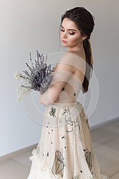 Beautiful brunette girl in elegant dress with long train with lavender flowers
