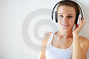 Beautiful brunette girl with headphones listening to music while sitting on the floor in an empty room on the white wall