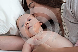 Beautiful brunette girl kissing her baby. They`re in the bedroom. The concept of love and happiness