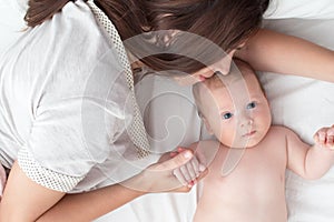 Beautiful brunette girl kissing her baby. They`re in the bedroom. The concept of love and happiness