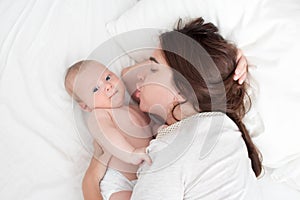 Beautiful brunette girl kissing her baby. They`re in the bedroom. The concept of love and happiness