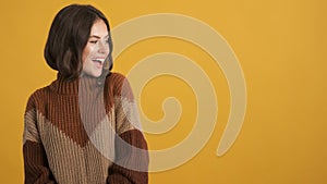 Beautiful brunette girl in knitted sweater happily looking aside on copy space over colorful background