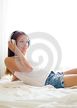 Beautiful brunette girl listening to music on headphones in bed