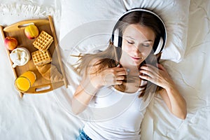 Beautiful brunette girl listening to music on headphones in bed