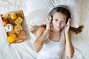 Beautiful brunette girl listening to music on headphones in bed . Breakfast Woman in the morning