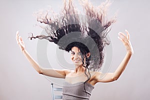 Beautiful brunette girl with long curly hair in the air, studio portrait. Happy smiling face expression