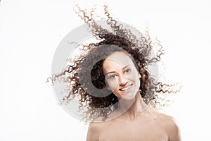 Beautiful brunette girl with long curly hair in the air, studio portrait. Happy smiling face expression