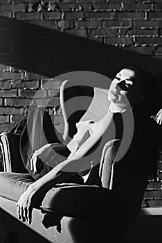 A beautiful brunette girl, a model in the studio. sun and shadow. sits on a chair. it is black the white photo. looks aside