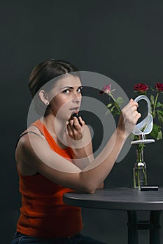 Beautiful brunette girl painting her lips at a coffee table, vertical photo