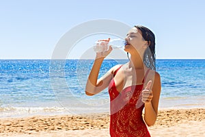 Beautiful brunette girl in red swimsuit drinking water on a vacation day