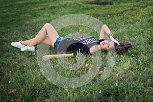 Beautiful brunette girl resting on lawn grass.a young bright teen girl loves sports.street fashion of contemporary youth girl