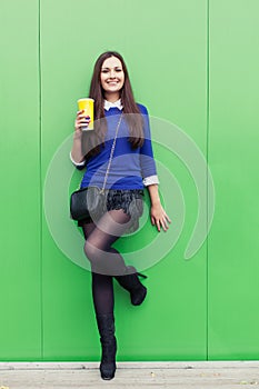 Beautiful brunette girl standing with a glass in his hand near the green wall and smiling at the camera