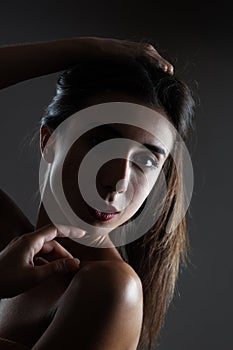 Beautiful brunette girl studio portrait. Side lit half silhouette on dark background. Serious face expression