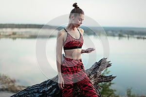 A beautiful brunette girl in stylish sports clothes is resting after a sport active workout near the lake. Listens to music on hea