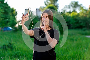 Beautiful brunette girl in summer outdoor. Talking on phone smiling showing sign gesture quietly. Listening to music