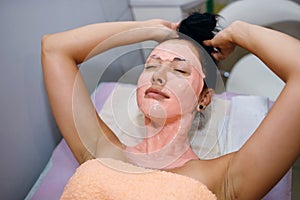 A beautiful brunette girl undergoes procedures in a spa salon, a master beautician applied a pink mask to her face