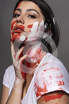 Beautiful brunette girl wearing a white t-shirt stained with paint touches her face and neck with her hand. Handprint of the palm