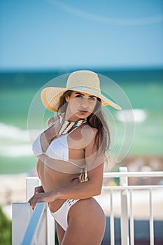 Beautiful brunette girl in a white bathing suit. Portrait of professional swimwear model posing provocatively outdoor
